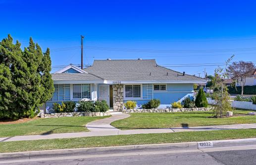Single-story suburban house with a well-kept lawn and clear blue sky.