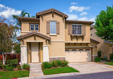 A modern two-story beige house with a three-car garage and a manicured front yard.