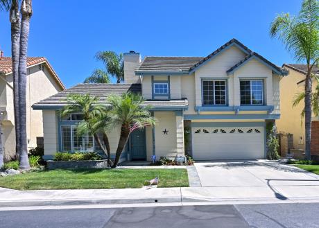 A modern two-story house with a well-kept lawn and palm trees.