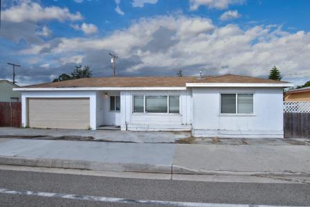 A single-story white house with a flat roof and a sidewalk in front.