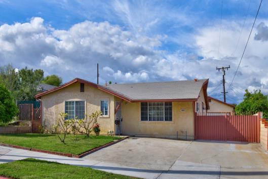Single-story suburban house with a driveway and garage under a partly cloudy sky.