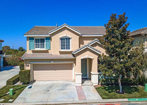 Two-story beige house with a driveway and a tree in front.