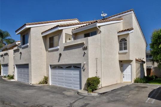 Two-story beige townhouse with a garage under a clear blue sky.