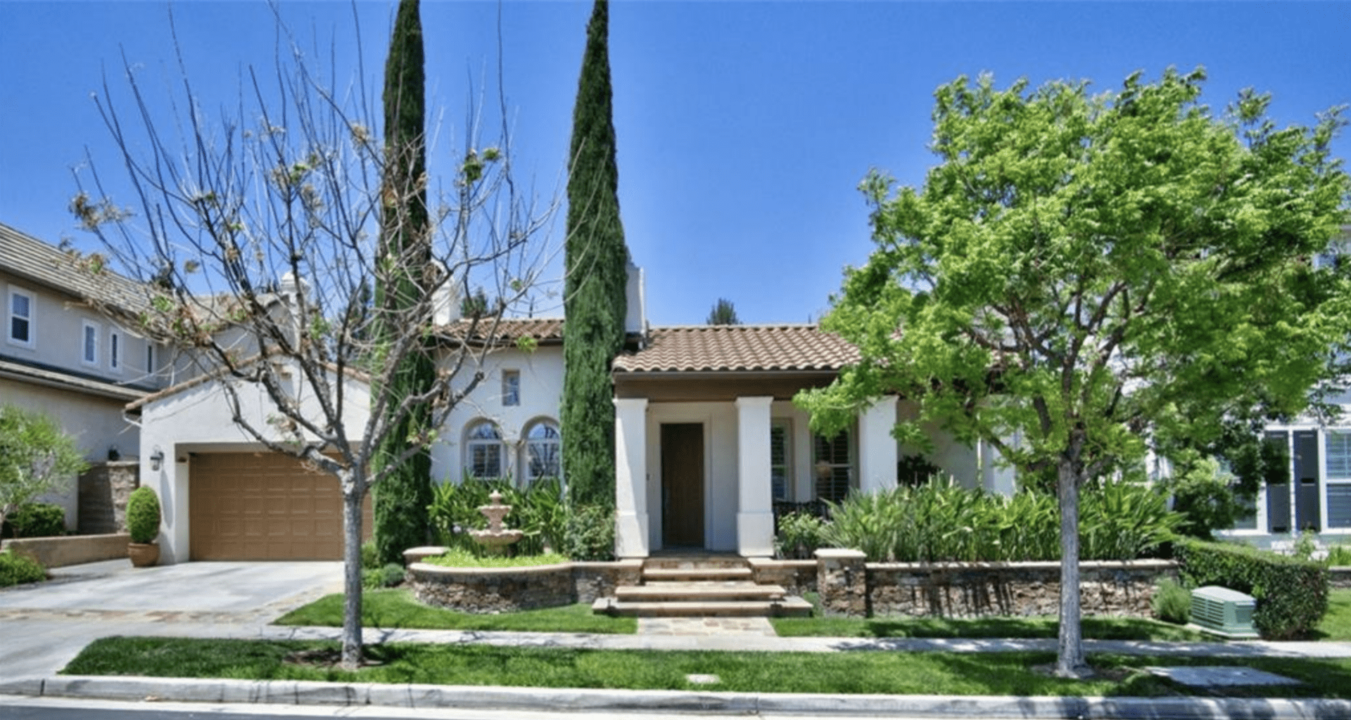 A charming Mediterranean-style house with tall cypress trees and a clear blue sky.