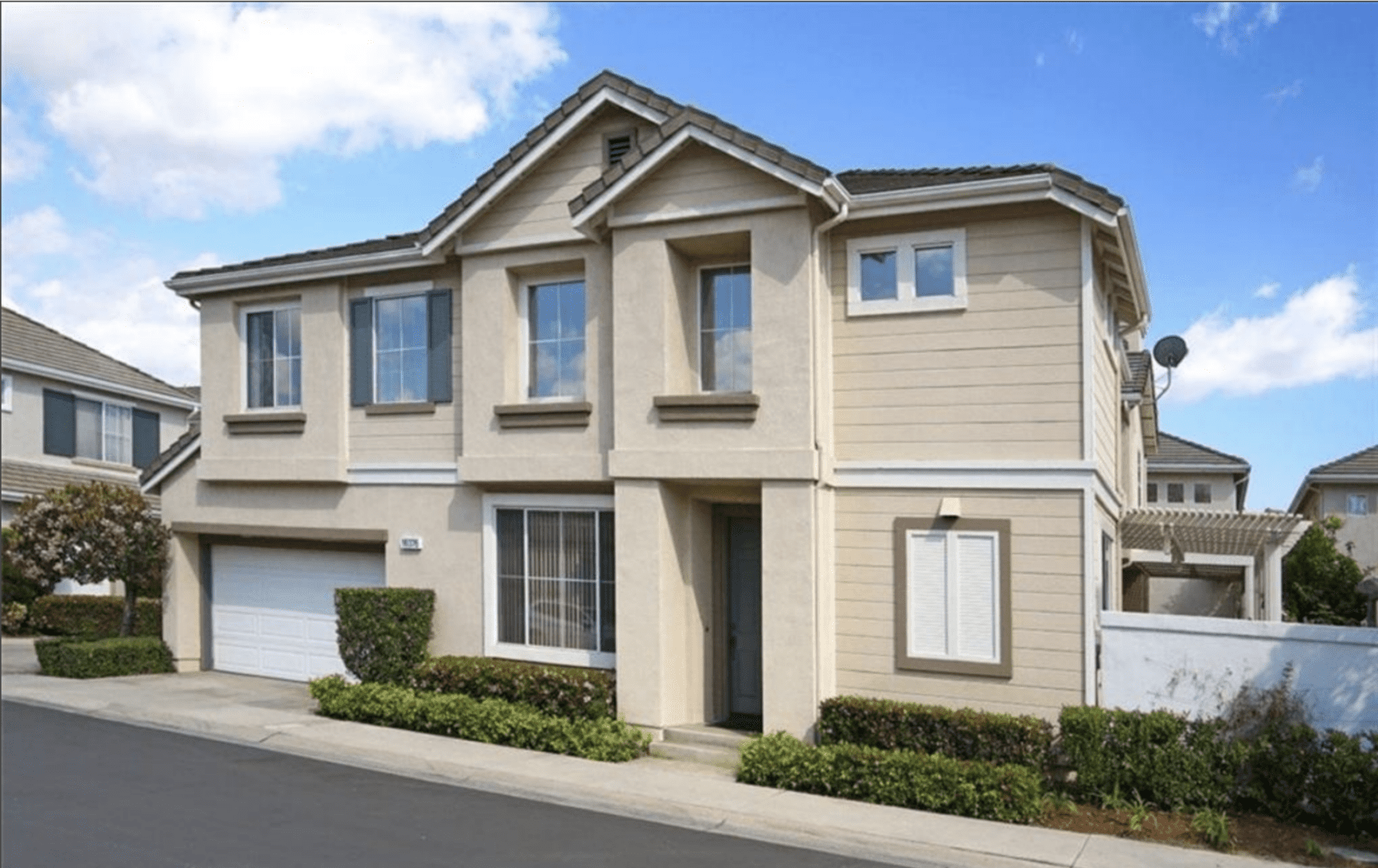 Modern beige townhouse with garages and neatly trimmed bushes.