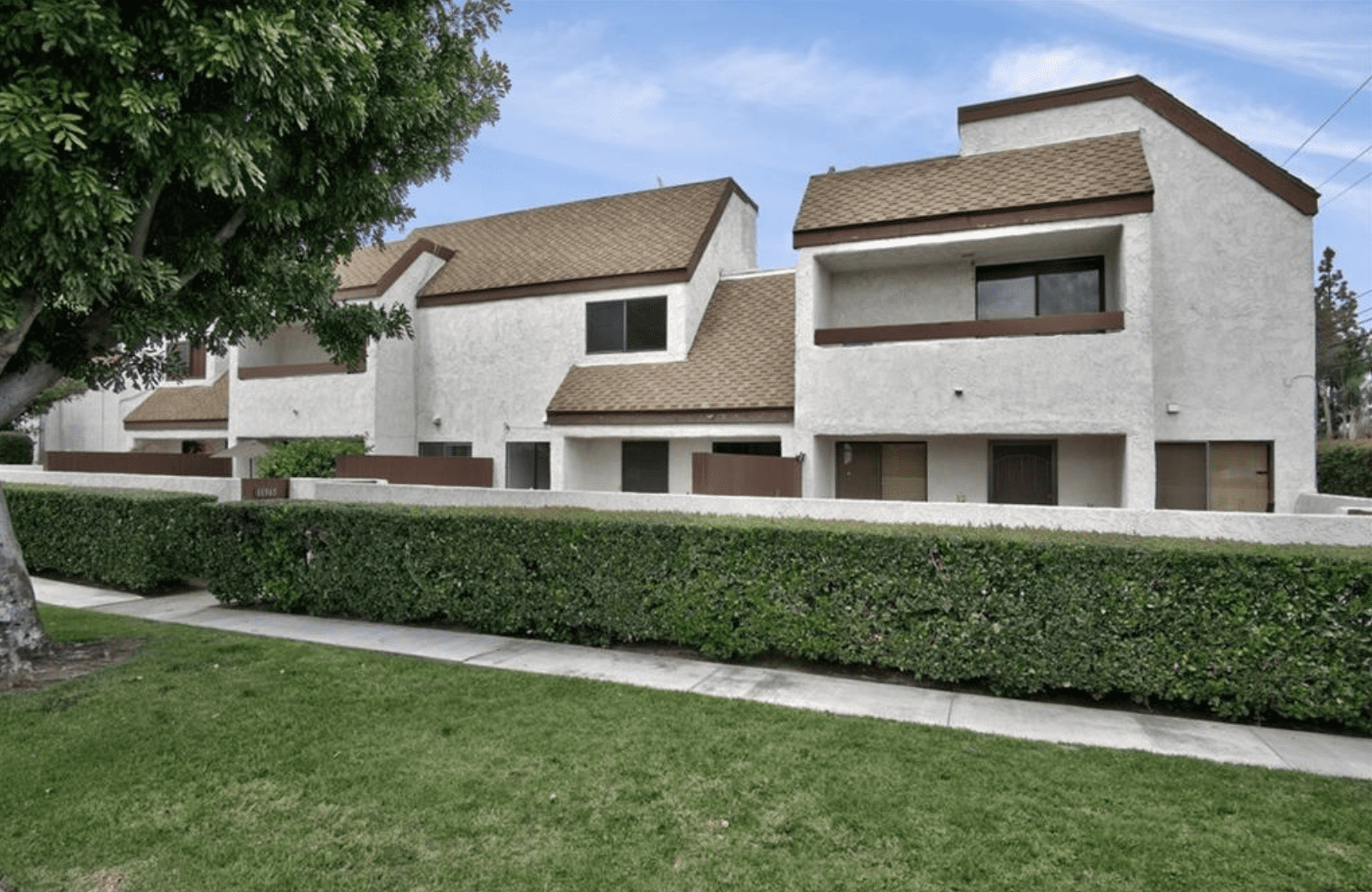 Modern white townhouses with brown shingled roofs and manicured hedges.