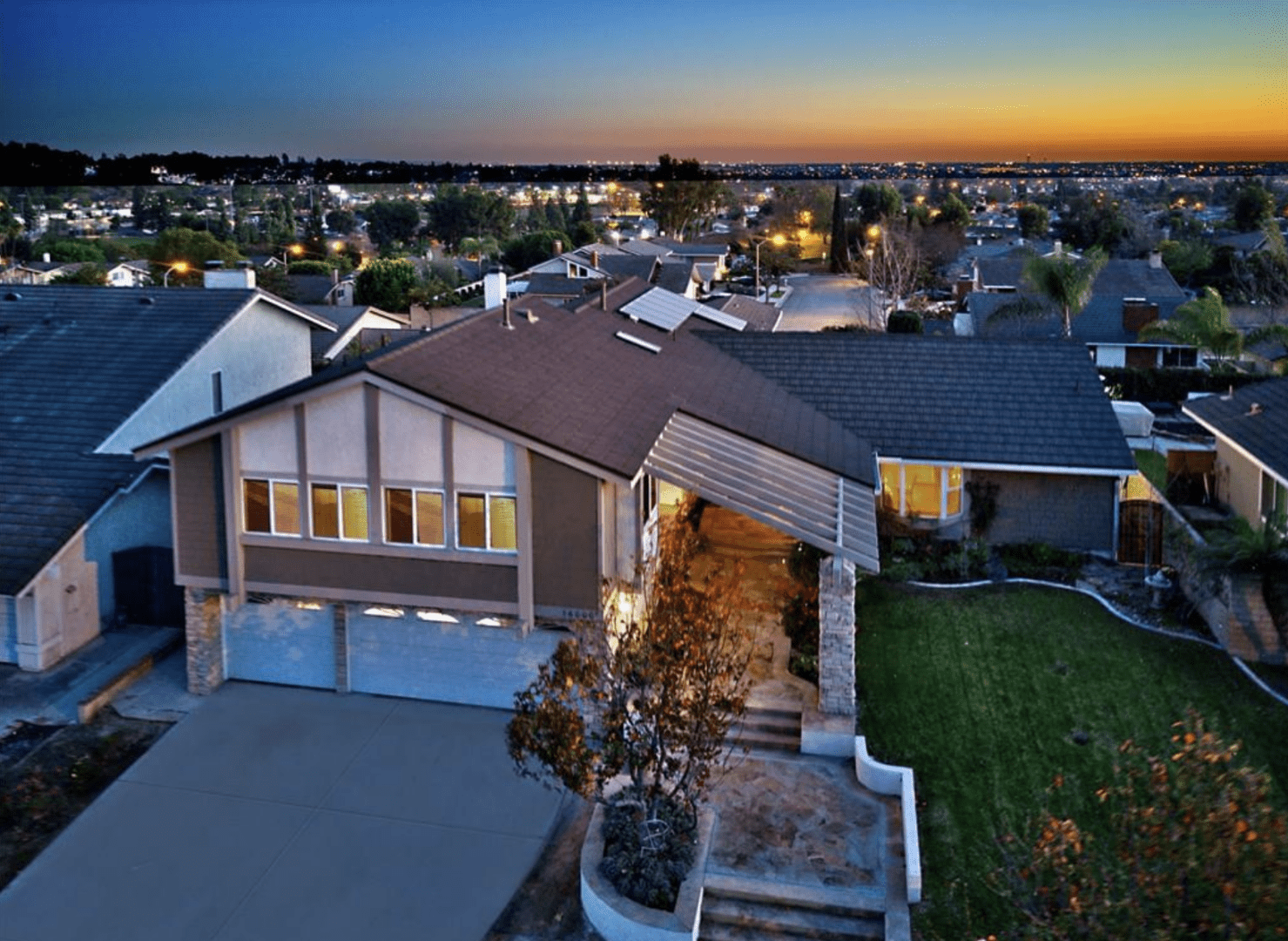 A modern suburban home at sunset with a well-lit exterior and landscaped yard.