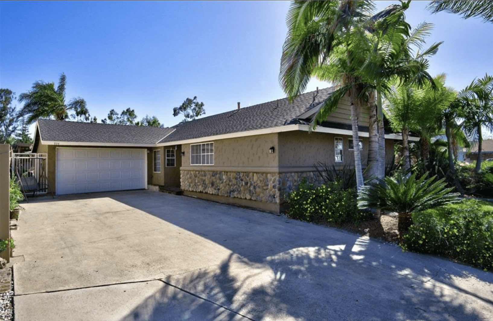 Single-story house with stone and brick exterior and palm trees.