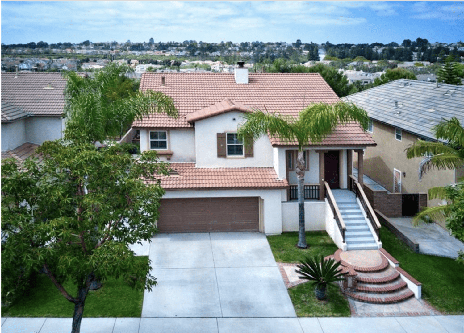 Modern two-story house with a tile roof and palm trees.