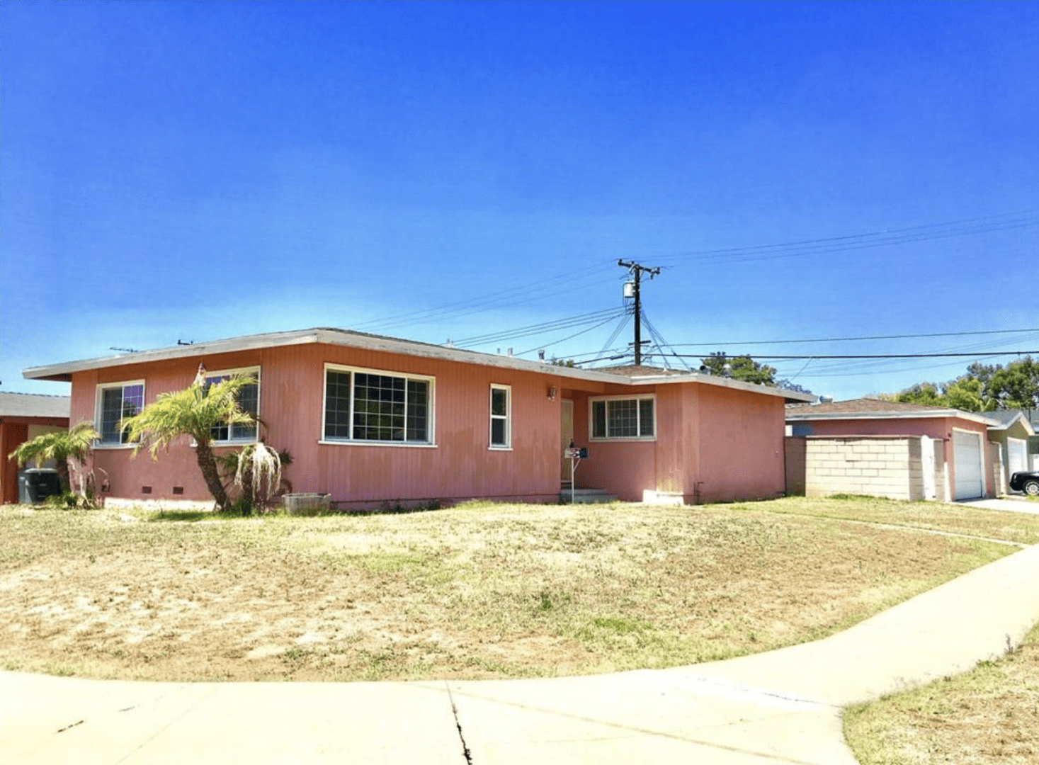 Single-story pink house with a dry lawn under a clear blue sky.