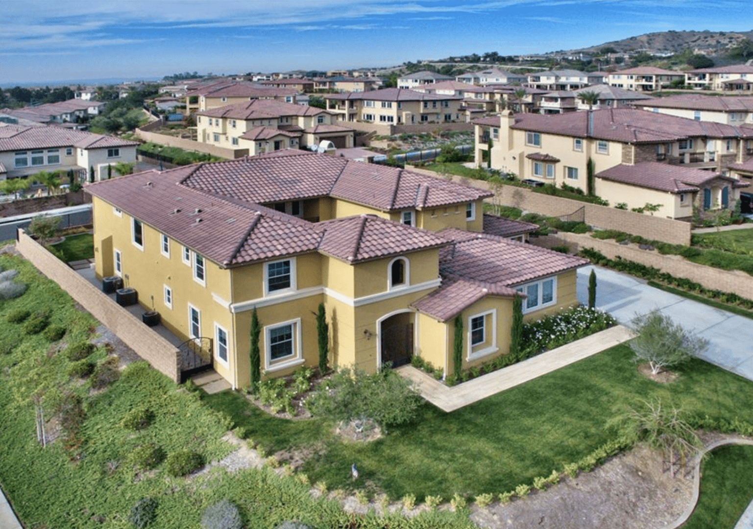 A beautiful yellow suburban house with a red tile roof and well-maintained lawn.